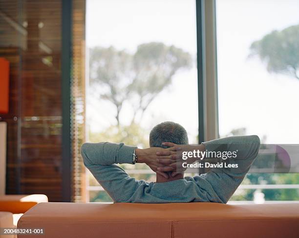 man sitting on couch with hands behind head, rear view - rear view hand window stock pictures, royalty-free photos & images