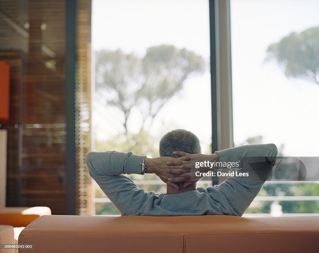 Man sitting on couch with hands behind head, rear view