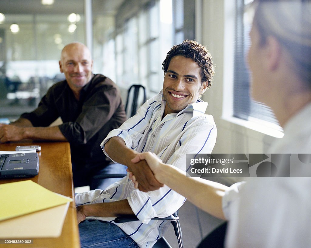 Businessman and businesswoman shaking hands at conference table