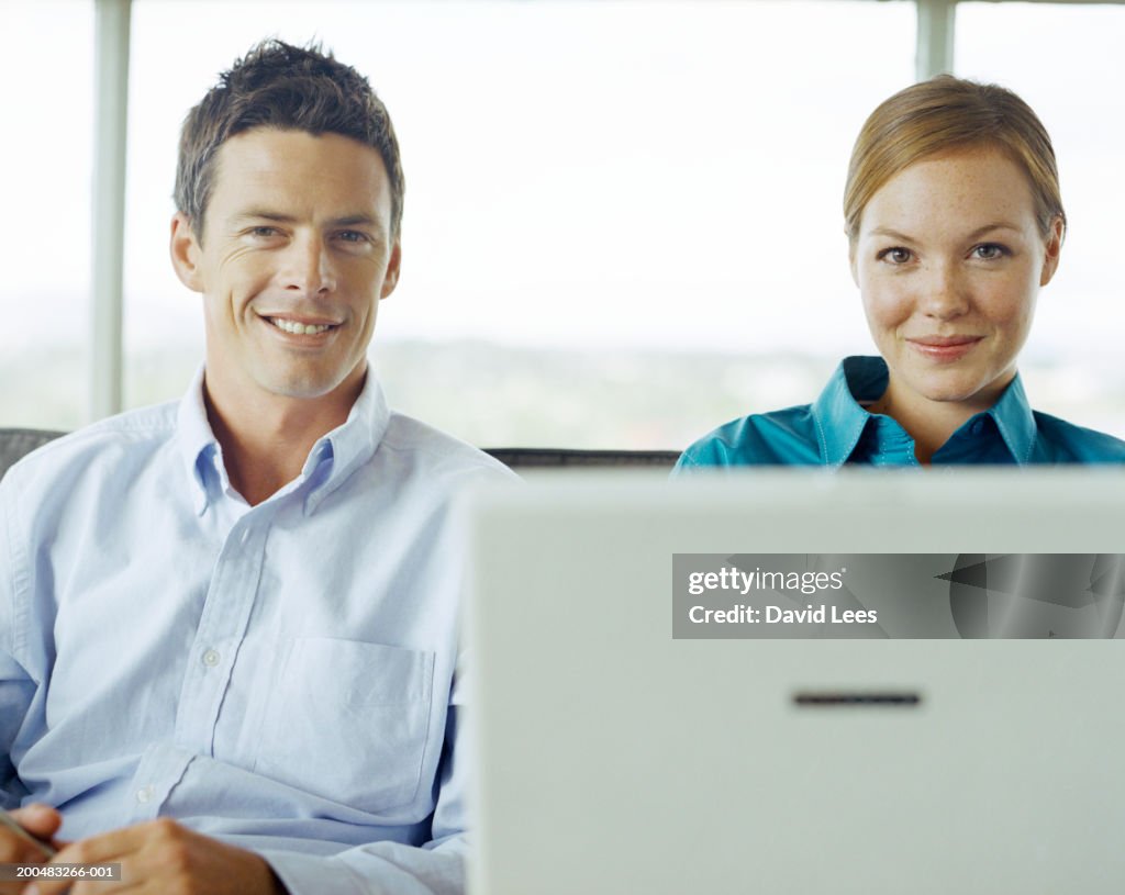 Man and woman sitting in front of laptop in office, portrait