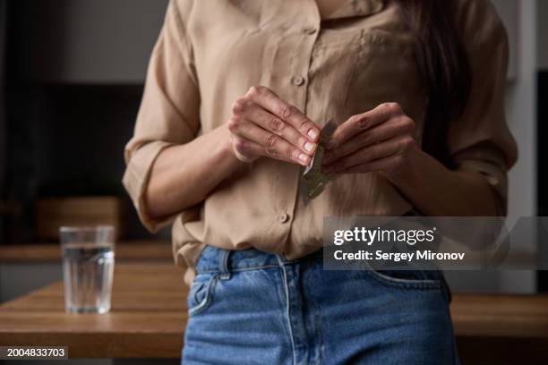 woman in casual clothing handling a pill blister pack with a focus on hand movements and a glass of water in the background. - hrt pill - fotografias e filmes do acervo