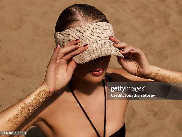 young woman on beach, wearing sun visor, elevated view - sonnenbaden stock-fotos und bilder