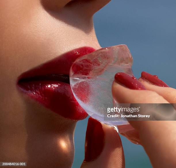 young woman holding ice cube to lips, close-up - freezing hands stock-fotos und bilder