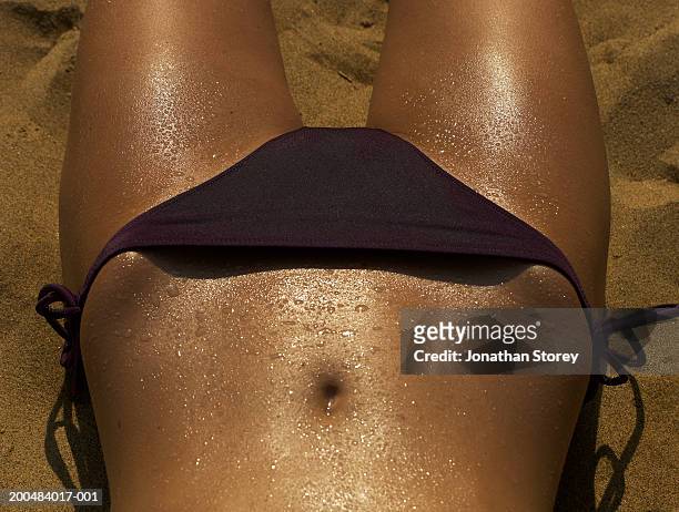 young woman lying on beach, skin glistening with water droplets - belly button stock pictures, royalty-free photos & images