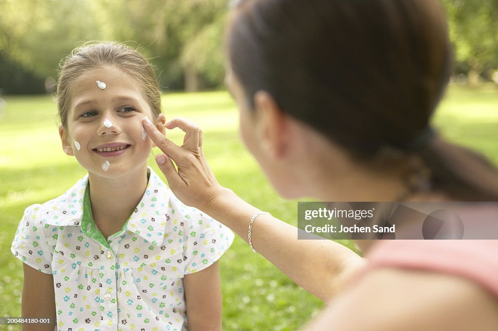 "Mother applying sun lotion to daughter's (7-9) face, outdoors"