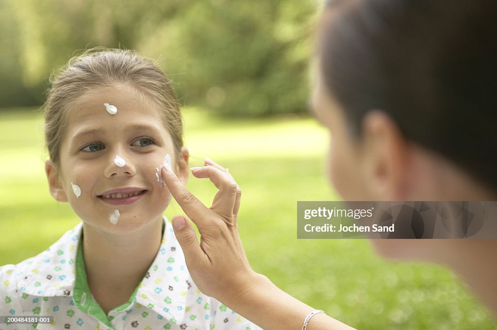 Mother applying sun lotion to daughter's (7-9) face, outdoors