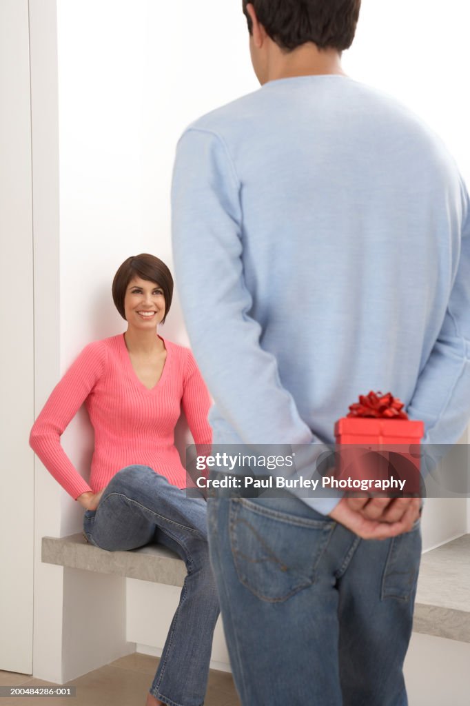 Young man standing in front of young woman, hiding present behind back