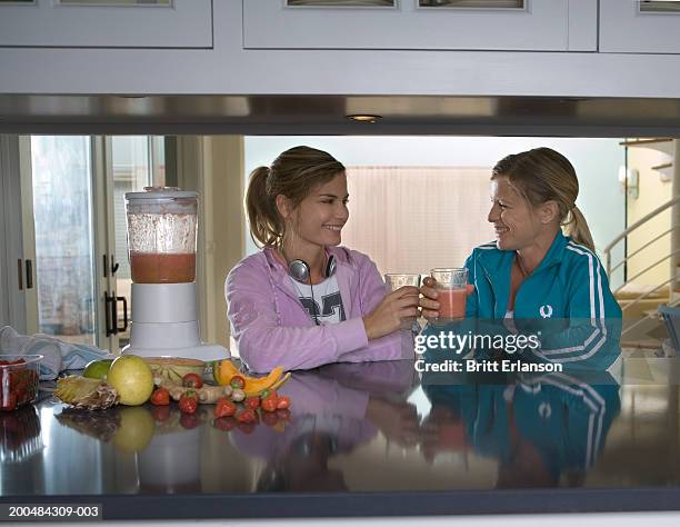 young woman drinking smoothie with mother, smiling at each other - ginger glasses stock-fotos und bilder