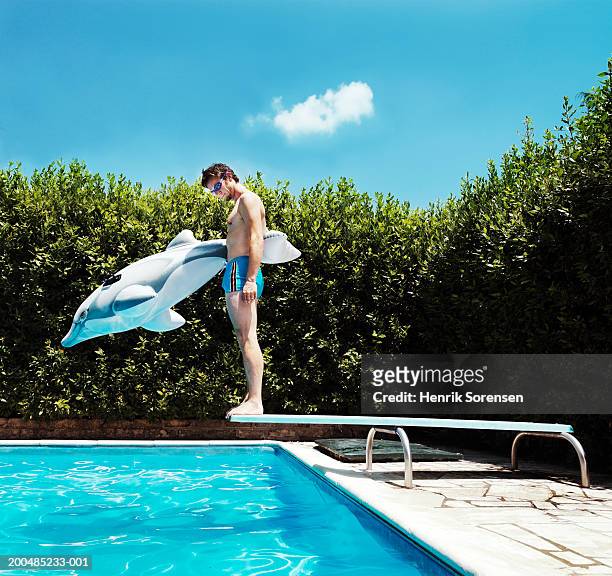 man standing on springboard beside pool with inflatable toy dolphin - diving board stock pictures, royalty-free photos & images