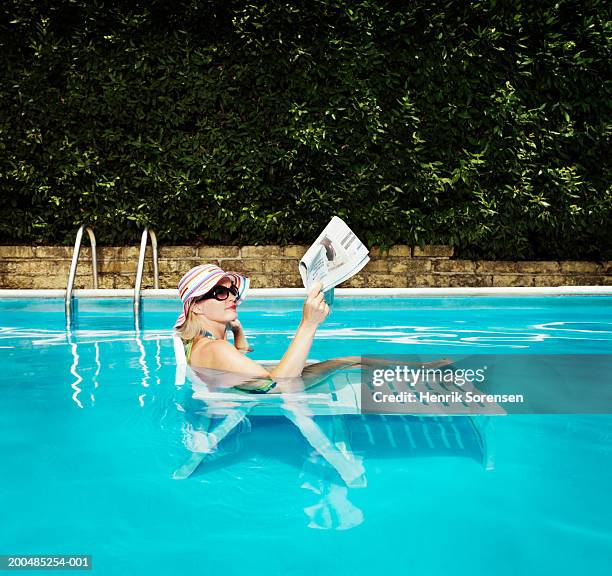 woman in sun hat relaxing on sunlounger in pool, reading newspaper - paper pool stock pictures, royalty-free photos & images