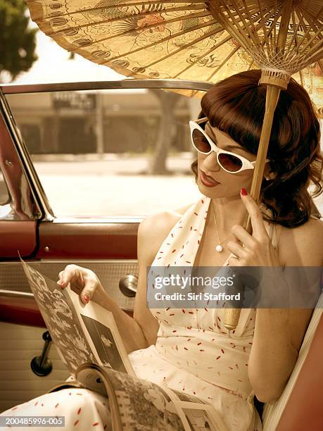 woman in 50's style dress  carrying parasol in vintage car - vintage 1950s woman stock pictures, royalty-free photos & images