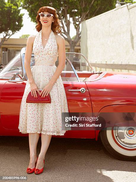 woman in 50's style dress  standing next to vintage car - white handbag stockfoto's en -beelden