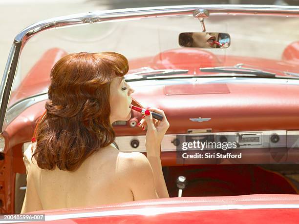 woman in 50's style dress putting on lipstick in vintage car - olden foto e immagini stock