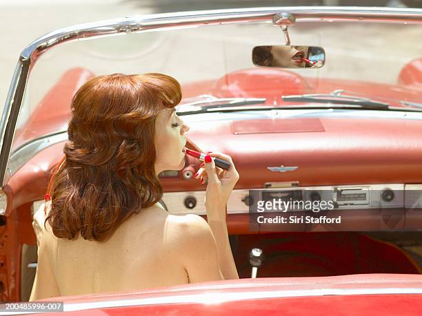 woman in 50's style dress  putting on lipstick in vintage car - anos 50 imagens e fotografias de stock