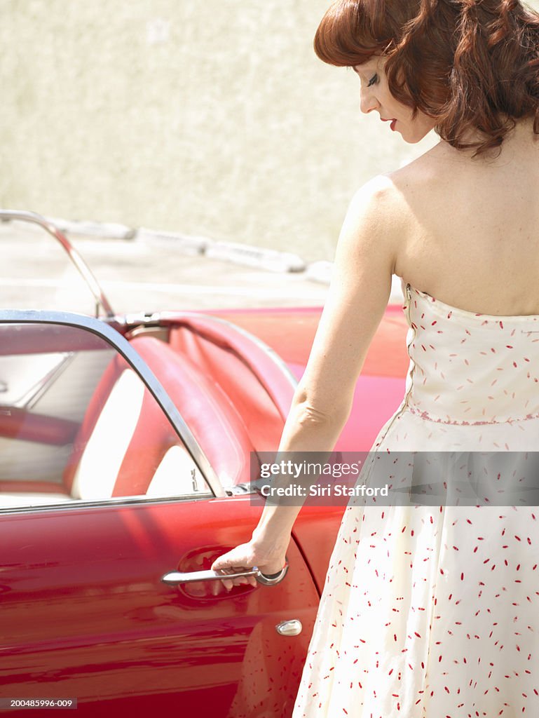 Woman in 50's style dress  opening vintage car door