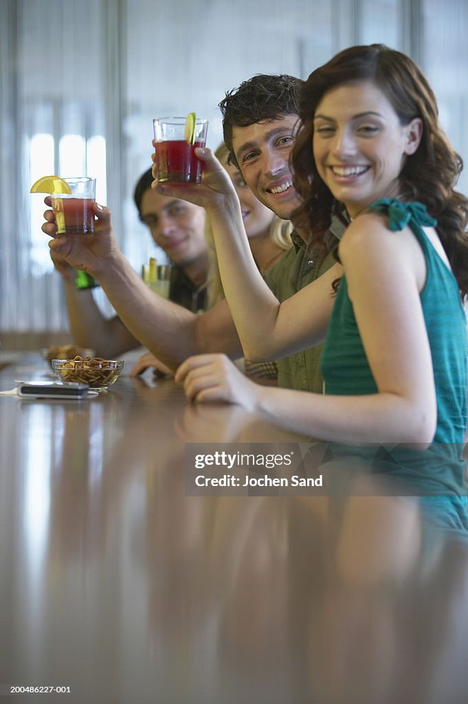 Four friends holding cocktails at bar, smiling, portrait