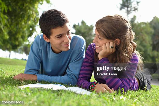 teenage couple (13-17) lying on grass, reading textbook, smiling - teen dating stock pictures, royalty-free photos & images