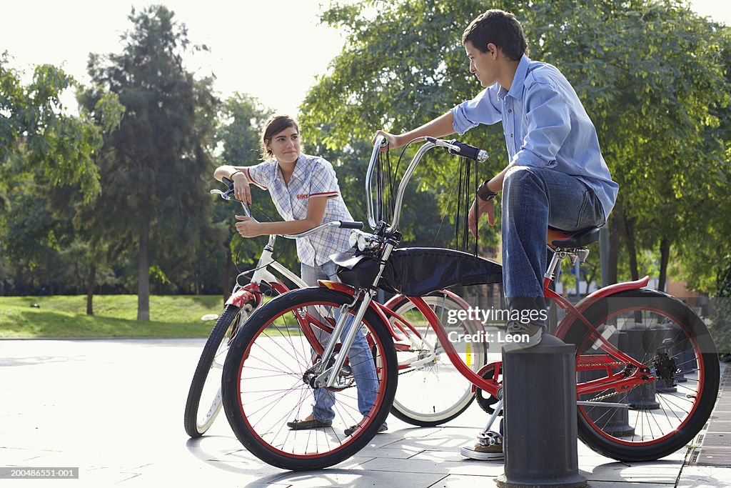 Teenage couple (13-17) sitting on bikes in park, smiling