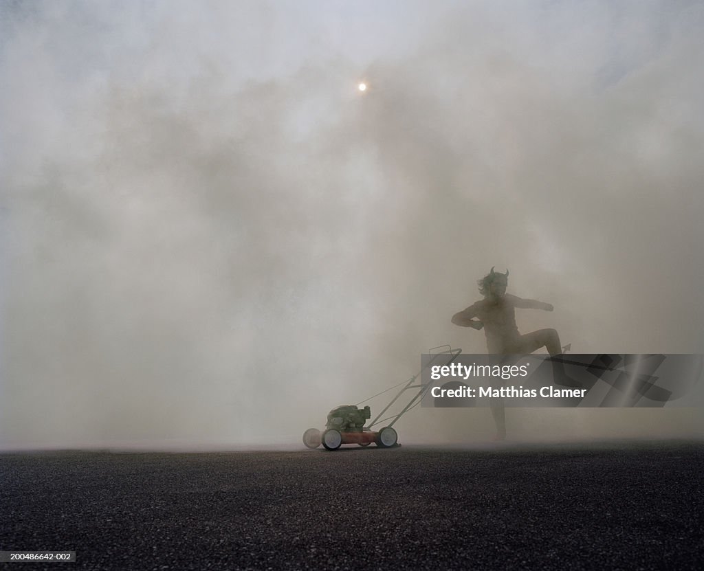 Man in devil's costume dancing next to lawn mower in smoke