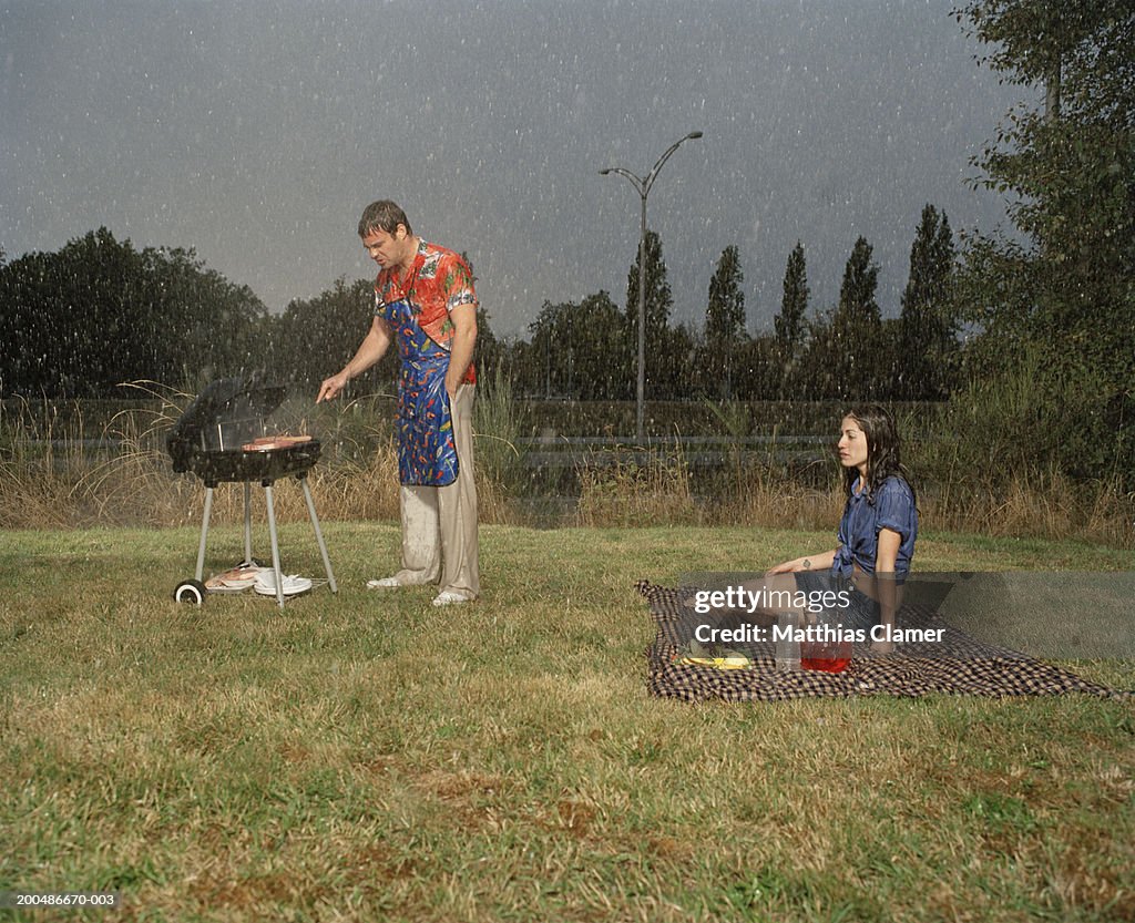 Couple having picnic in rain, man grilling meat