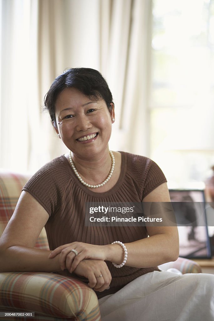 Mature woman sitting at home, smiling, portrait