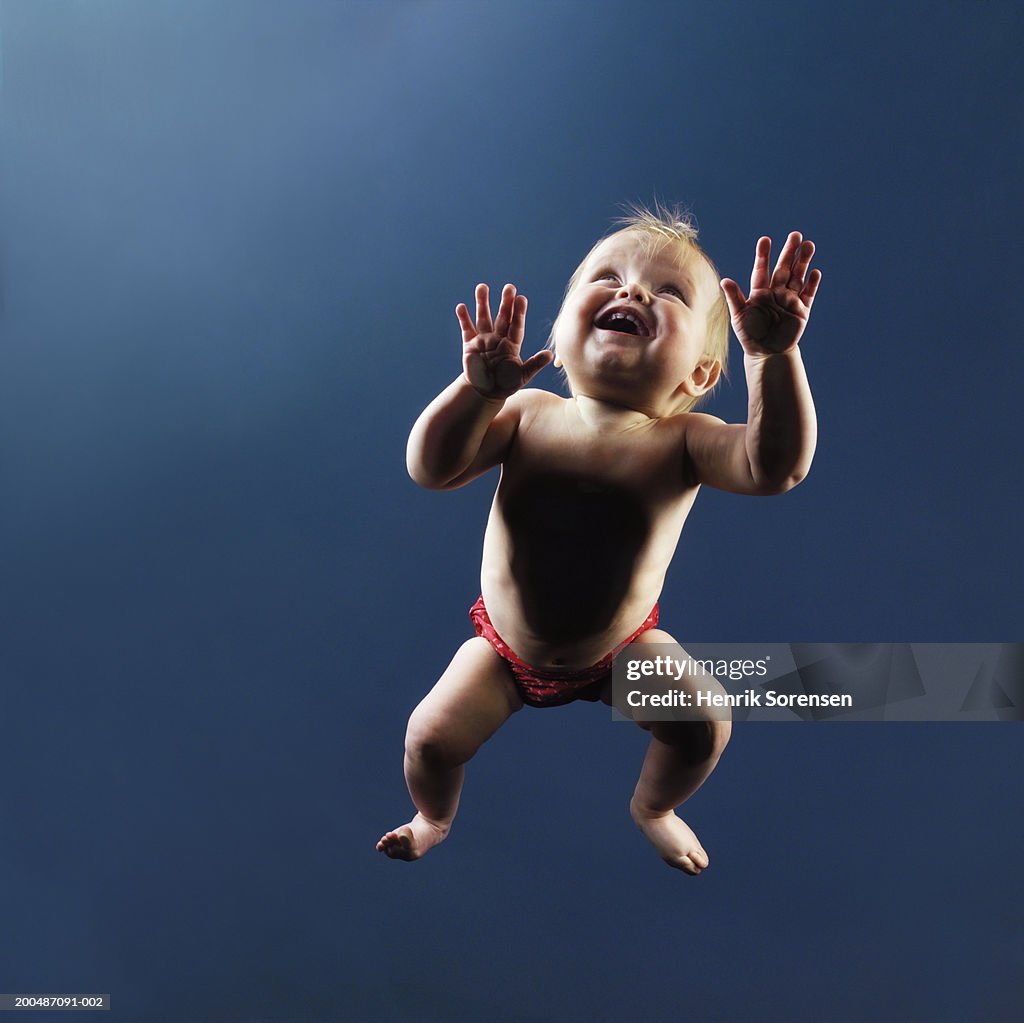 Baby girl (9-12 months) crawling on glass pane, view from below