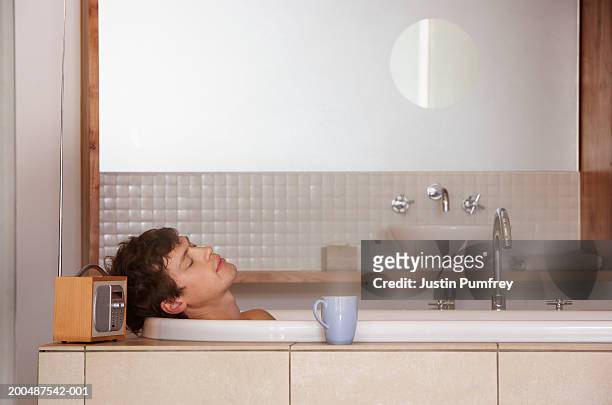 young man relaxing in bath, side view - radio hören stock-fotos und bilder