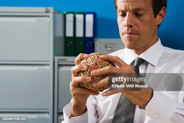 businessman holding ball of elastic bands in office - elastic band ball stock pictures, royalty-free photos & images