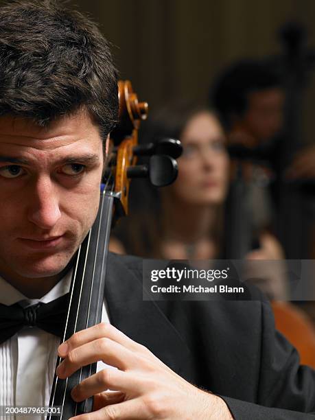 male cellist performing in orchestra, focus on foreground - violoncello foto e immagini stock