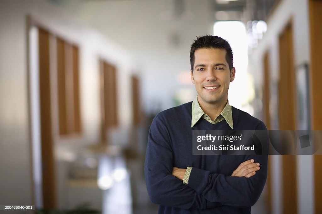 Businessman standing in hallway of office, arms crossed