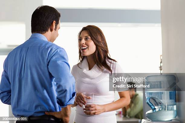 young man talking to female colleague by watercooler - water cooler stock pictures, royalty-free photos & images