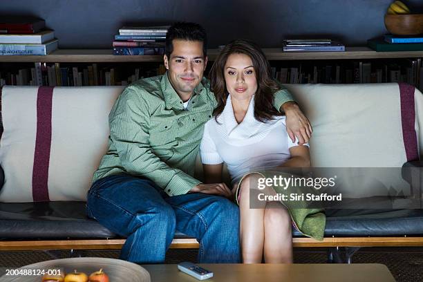 young couple sitting on couch watching television - een dag uit het leven serie stockfoto's en -beelden