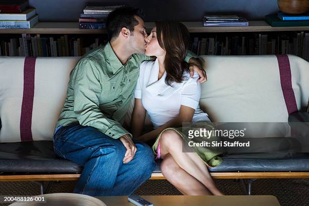 young couple kissing in front of television - couple kissing stock pictures, royalty-free photos & images