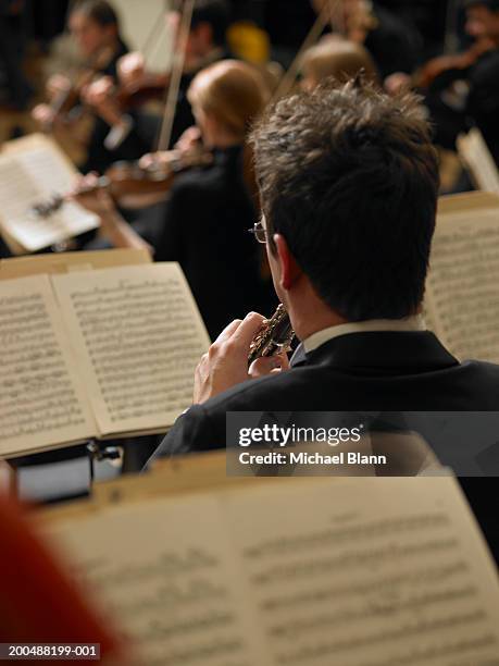 man playing oboe in orchestra, violinists in background, rear view - oboe stock-fotos und bilder