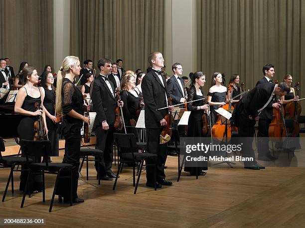 orchestra standing at end of concert, conductor bowing - bow musical equipment stock pictures, royalty-free photos & images