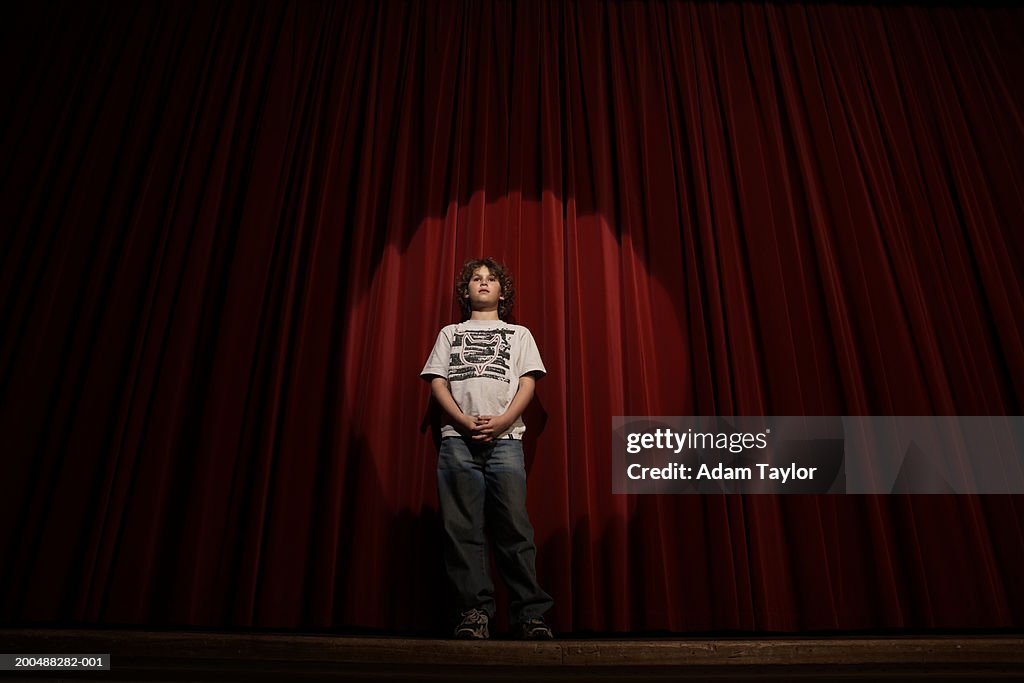 Spotlight on boy (10-12)  standing on stage curtains, low angle view