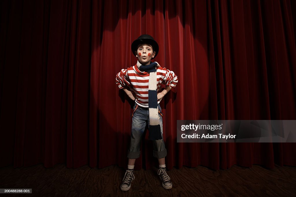 Spotlight on boy (8-10)  wearing clown outfit, hands on hips, portrait