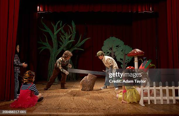 two boys (9-11) acting as lumberjacks on stage, sawing tree stump - recita della scuola foto e immagini stock