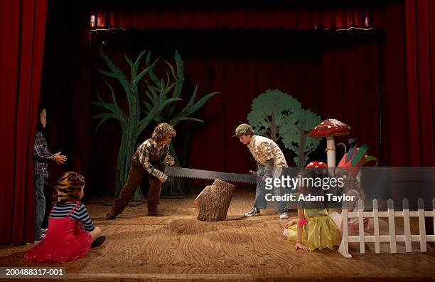 two boys (9-11) acting as lumberjacks on stage, sawing tree stump - school play 個照片及圖片檔
