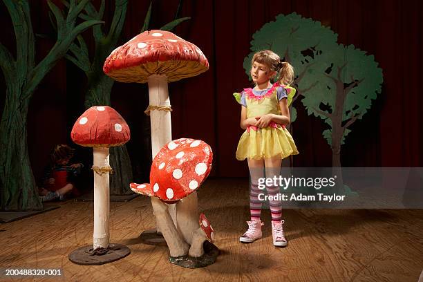 girl (5-7) standing beside giant toadstools on stage - school play 個照片及圖片檔