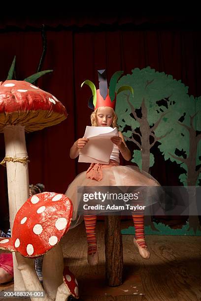 girl (4-6) on stage, sitting on giant toadstool practicing lines - school play 個照片及圖片檔