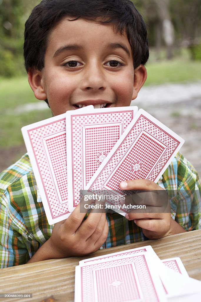 Boy (6-8) jugando con tarjetas en mesa de jardín; Primer plano; Vertical