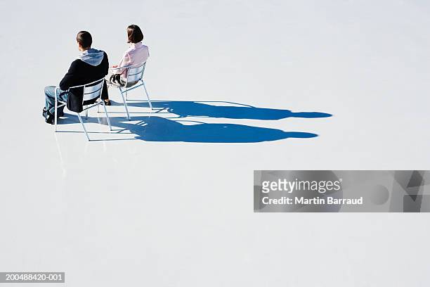 man and woman sitting on aluminium chairs on platform, rear view - chaise de dos photos et images de collection