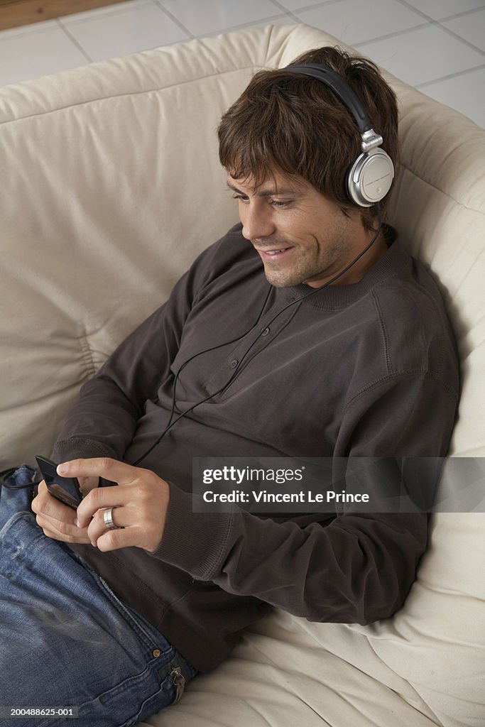 Young man on sofa listening to headphones, elevated view