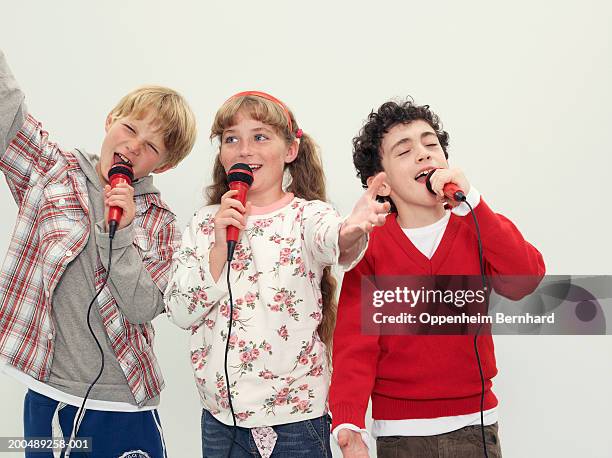 two boys (8-10) and girl (9-11) singing into microphones - boy singing stock-fotos und bilder