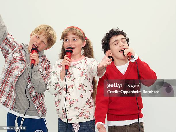 two boys (8-10) and girl (9-11) singing into microphones - boy singing stock pictures, royalty-free photos & images