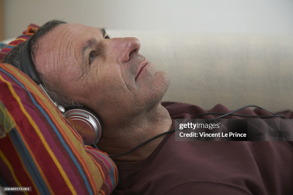 Mature man lying on sofa listening to headphones, close-up, side view