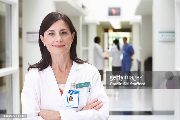 mature female doctor standing in hallway, arms crossed - namensschild stock-fotos und bilder