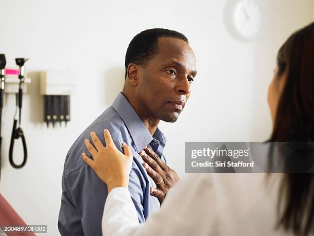 female doctor talking to  patient in examination room - man touching shoulder stock-fotos und bilder