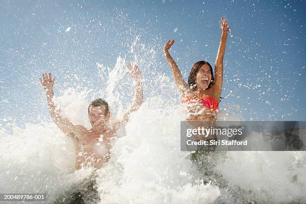 young couple jumping against waves - jumping into water stock pictures, royalty-free photos & images